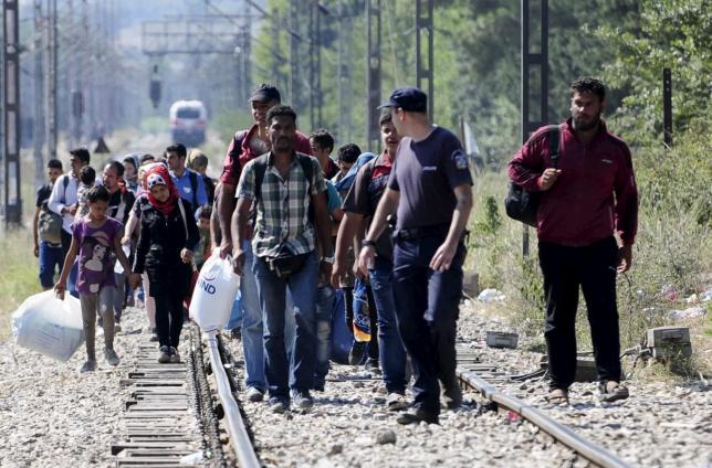 A Greek police officer guides migrants arriving to enter Macedonia, near the border with Greece, August 27, 2015. Migrants are trekking from the southern Macedonian border near Gevhelija to the northern border with Serbia on their way to Western Europe. REUTERS/Ognen Teofilovski