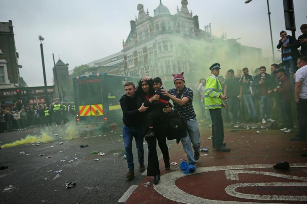 LONDON, ENGLAND - MAY 10: A woman and a child are helped past West Ham fans as people become violent and start throwing bottles at police outside the Boleyn Ground on May 10, 2016 in London, England. Tonights Premier League match against Manchester United is West Ham United's last game at the Boleyn Ground, bringing to an end 112 years of the club's history at the ground. The club will move into the Olympic Stadium next season, making way for developers and plans for 800 new homes where the stadium now stands. (Photo by Dan Kitwood/Getty Images)